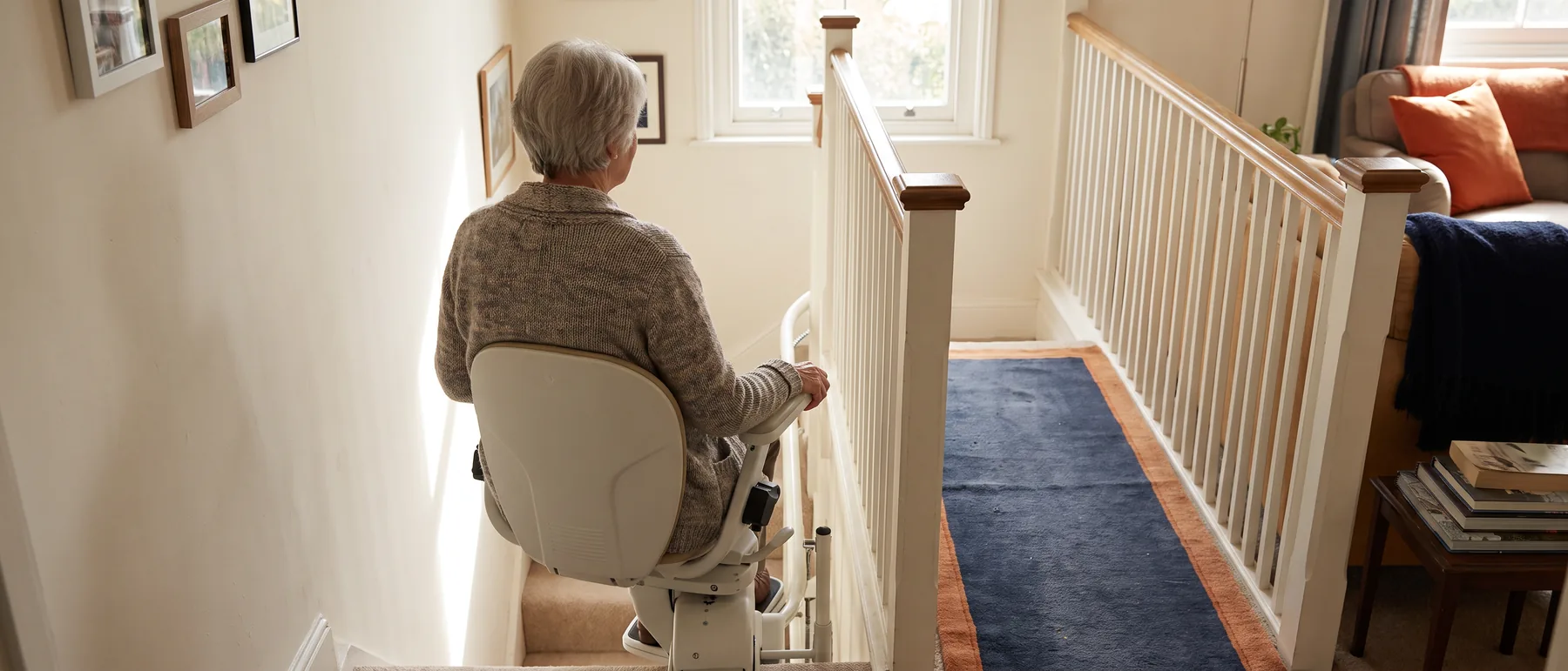 A woman riding a stair lift up a straight staircase at home